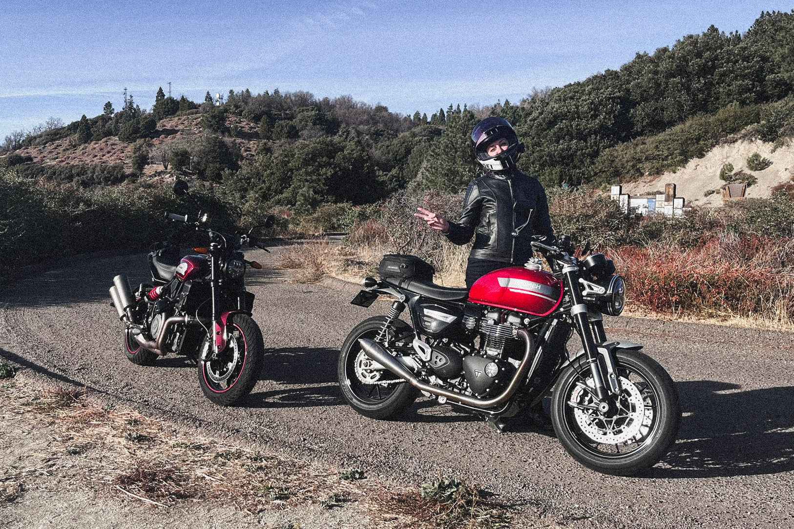 Woman standing beside two motorcycles in a casual outdoor Ratbag Moto lifestyle photo.