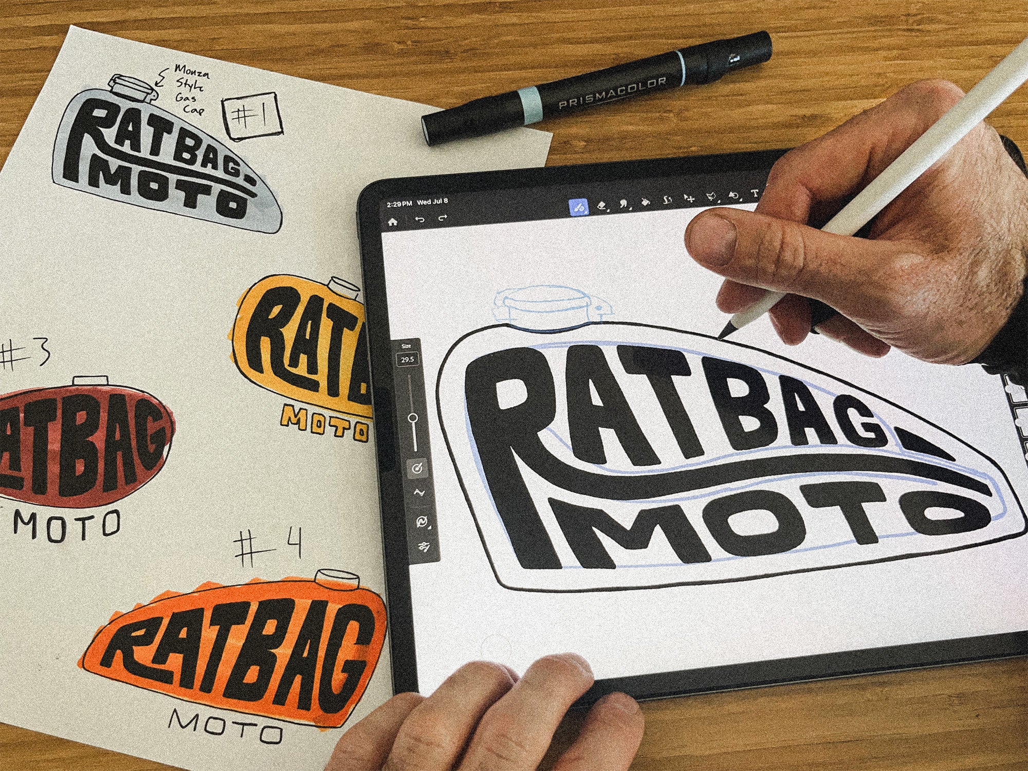 Hand drawing Ratbag Moto artwork on an iPad beside rough paper sketches of the Peanut Tank design.