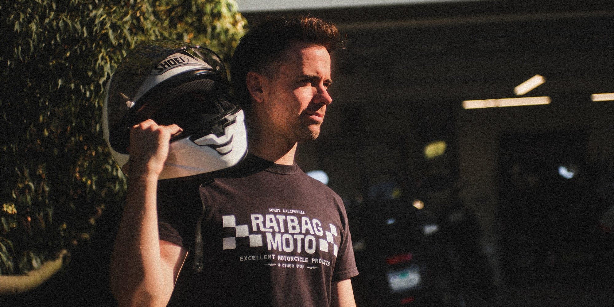 Ratbag Moto lifestyle photo outside an open garage with motorcycles in the background.